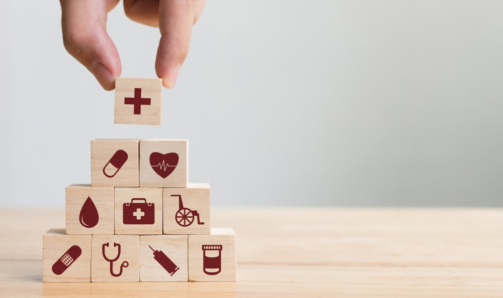 Person stacking wooden building blocks with various healthcare icons on them