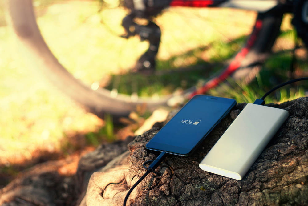 A cell phone and portable cell phone charger on a log in a park with a red bicycle in the background