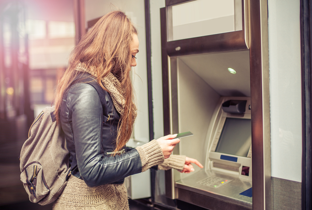Young woman with a backpack on withdrawing money from an ATM