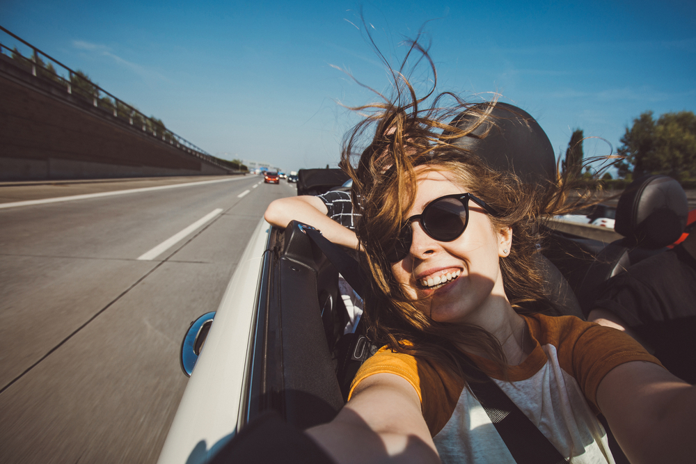 Young woman sitting in the passenger seat of a convertible and taking a selfie