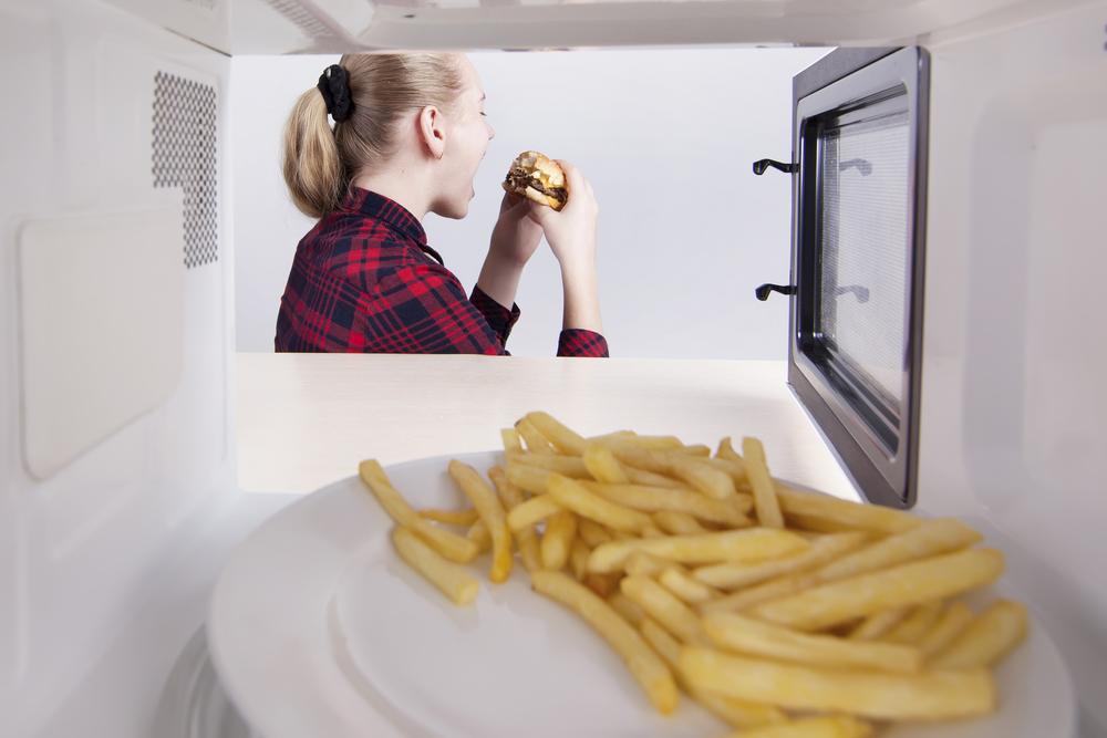 A young blonde student with a ponytail heating a burger and fries in the microwave